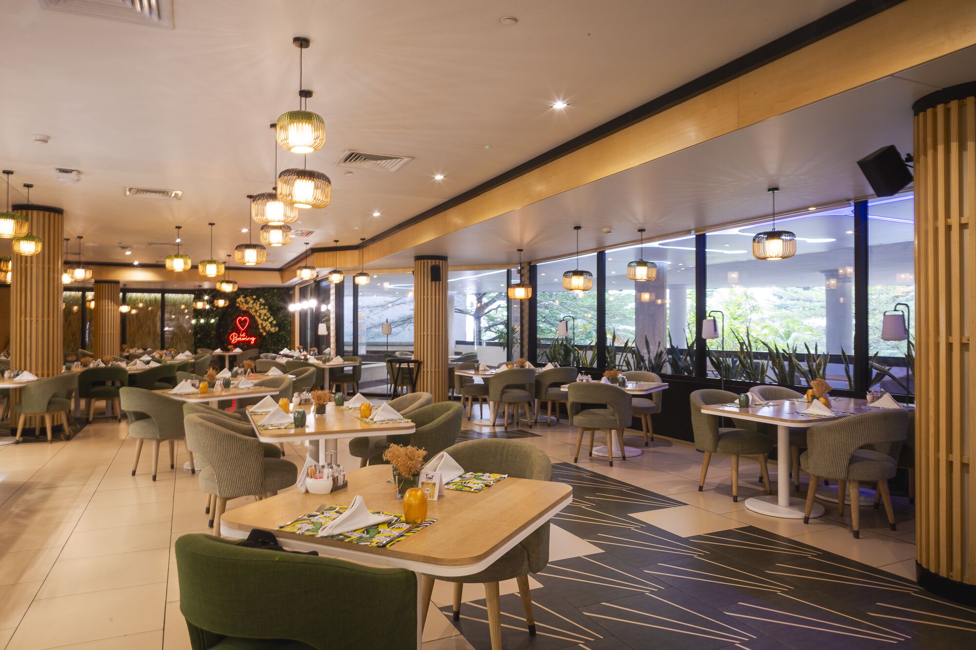 A restaurant with multiple tables and chairs, large windows, and hanging pendant lights.