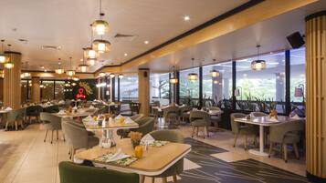 A restaurant with multiple tables and chairs, large windows, and hanging pendant lights.