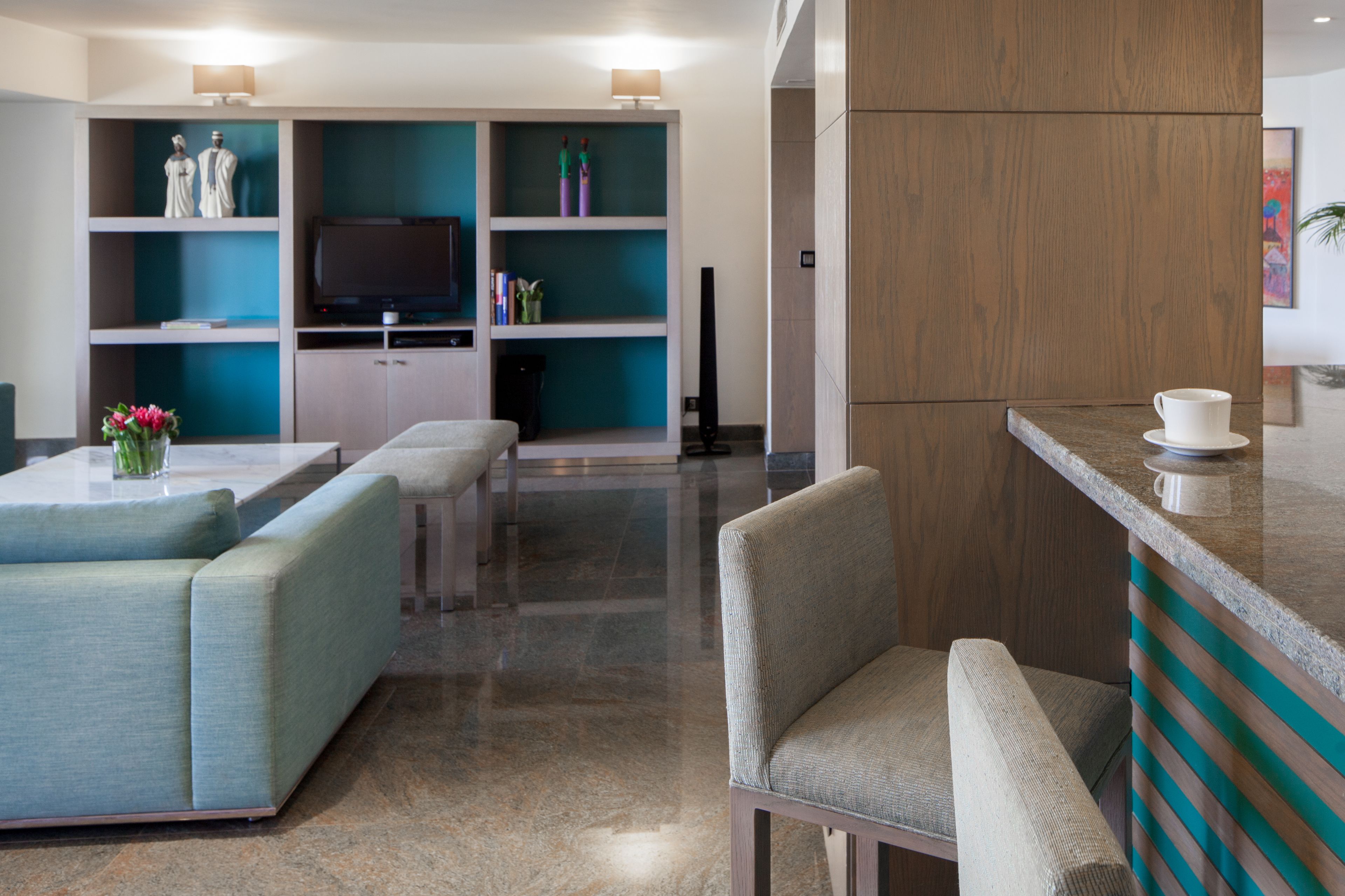 A modern living room with a sofa, a coffee table, and a TV on a stand. There are shelves with decorative items and a wooden cabinet.