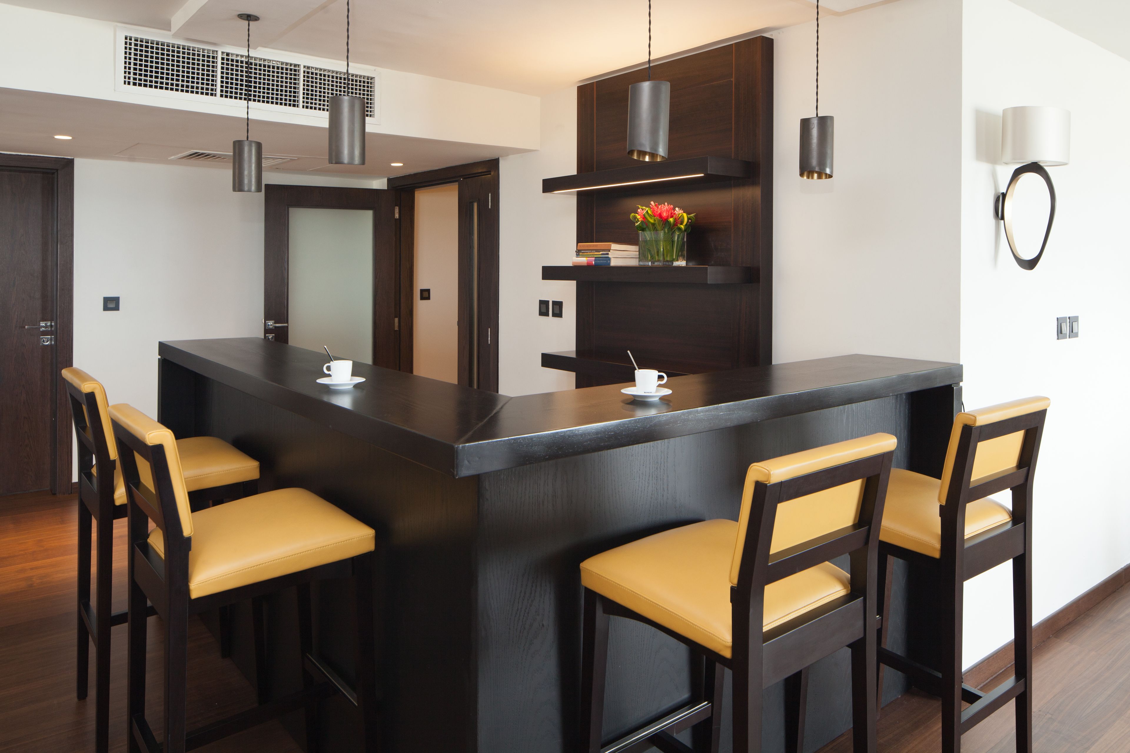 A modern kitchen with a central island, bar stools, pendant lighting, and a wall-mounted lamp.