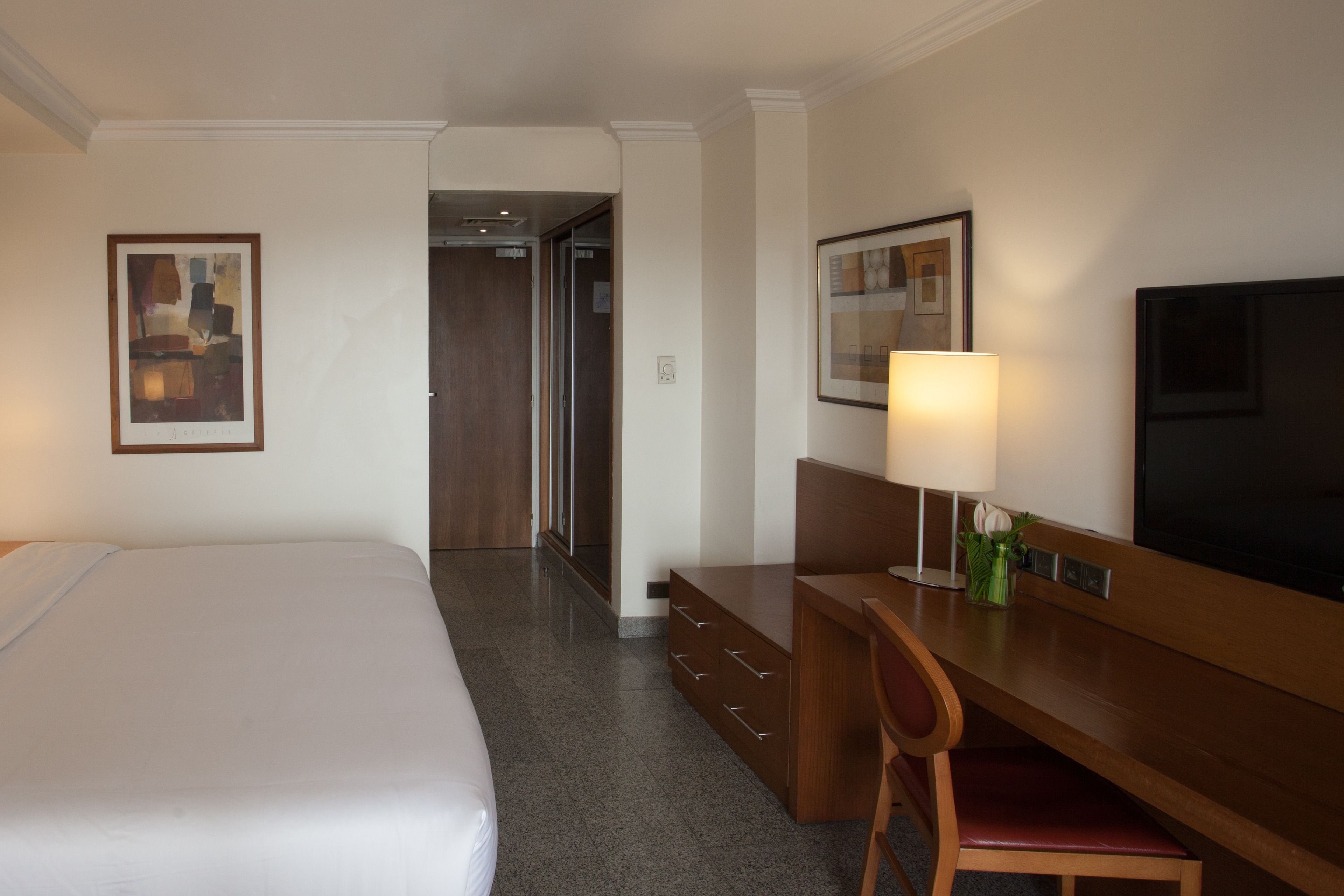 A hotel room with a large bed, a desk with a chair, a television, and artwork on the walls.
