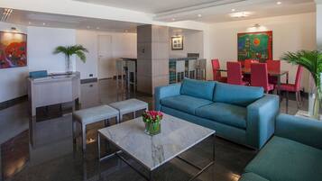 A modern hotel lobby with a blue sofa, a marble coffee table, and red chairs.