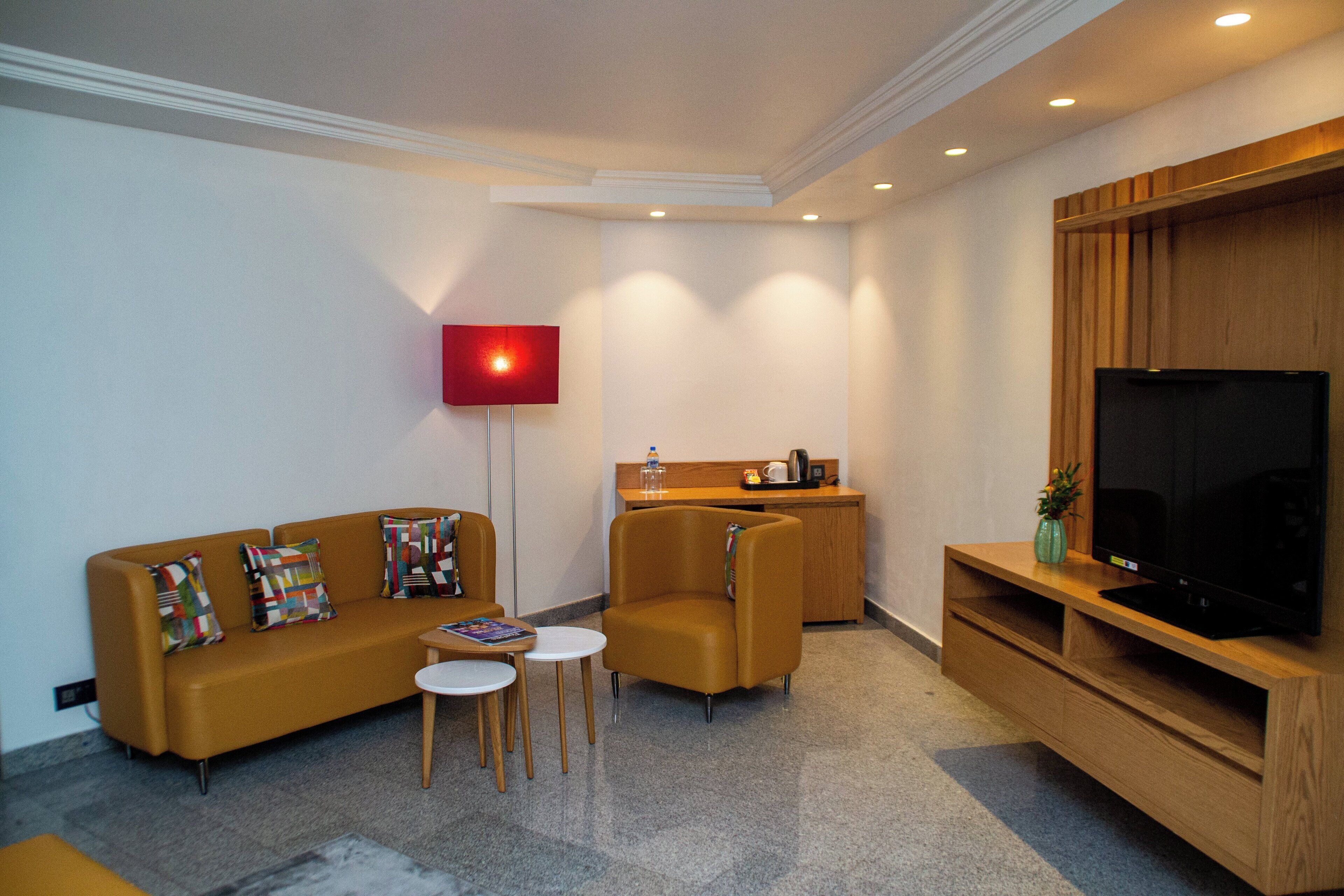 A modern living room with a sofa, armchair, coffee table, and a flat-screen TV on a wooden stand.