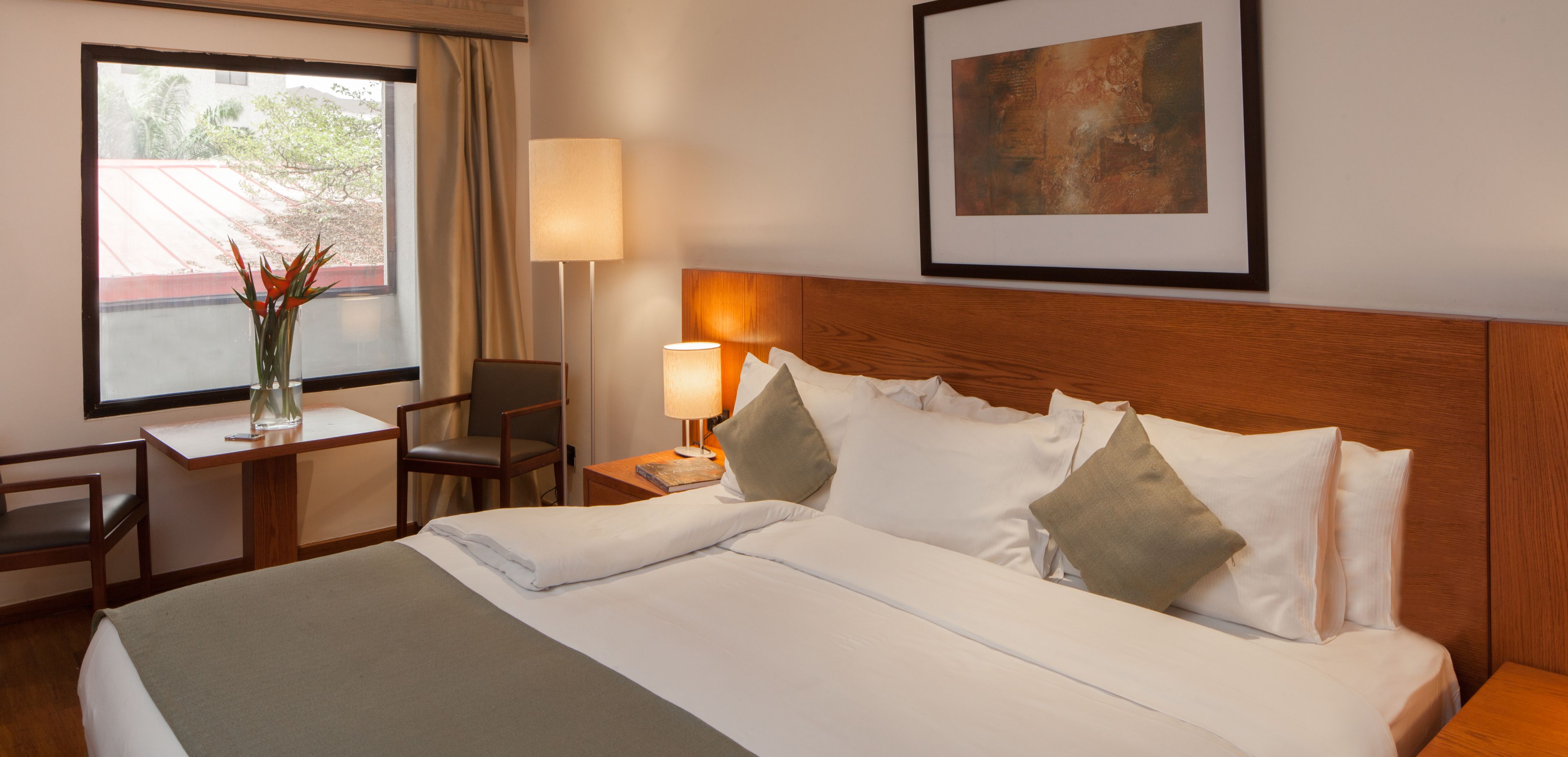 Une chambre d’hôtel avec un lit bien fait, un bureau avec une chaise, une lampe et un tableau encadré au mur.