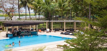 Piscina con sillas de descanso y una zona de bar, rodeada de palmeras y vistas al agua.