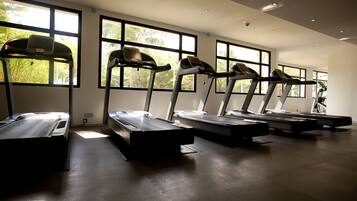 A gym with treadmills aligned against a wall with large windows.