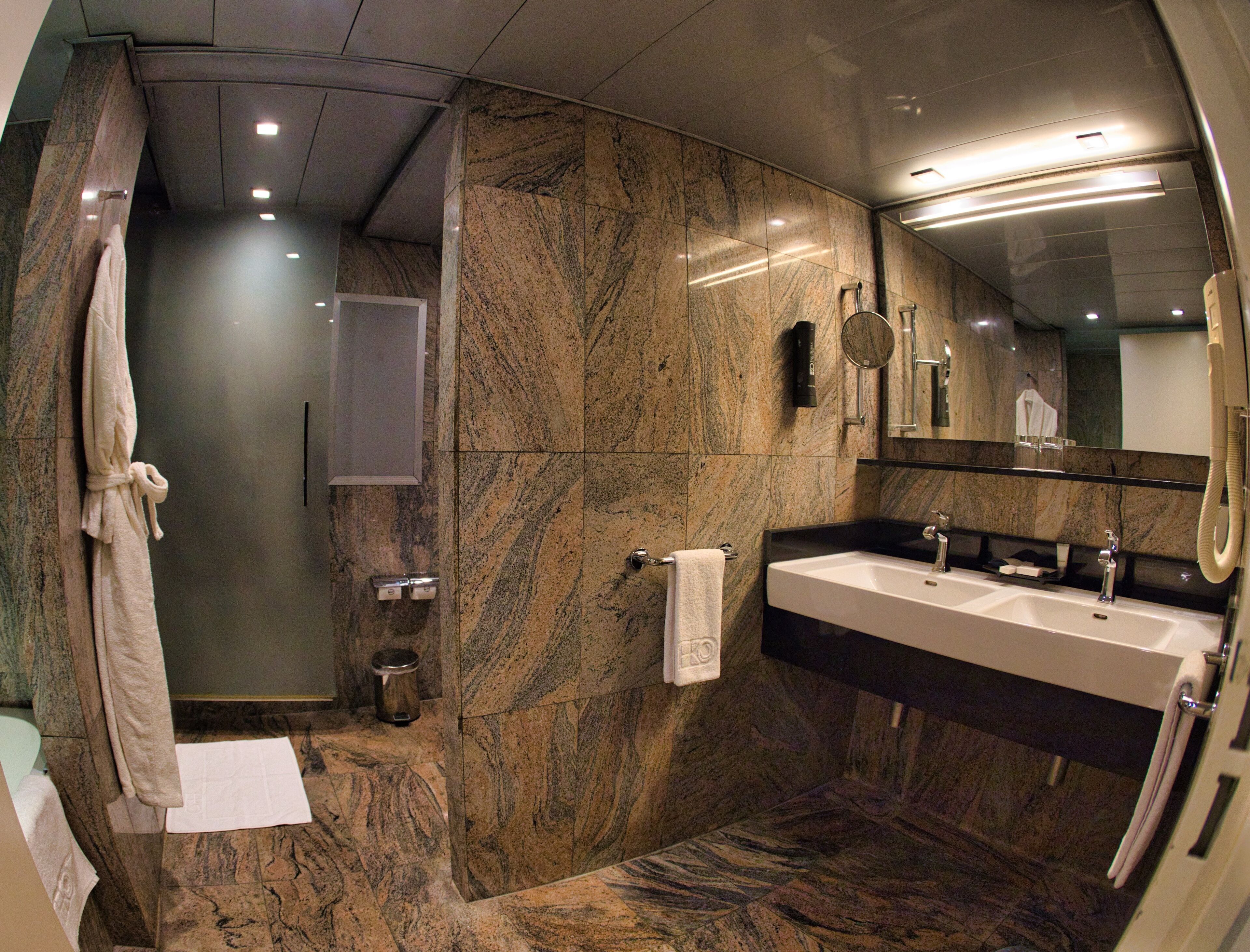 A modern bathroom with a marble floor, a large sink, a mirror, and a shower area.