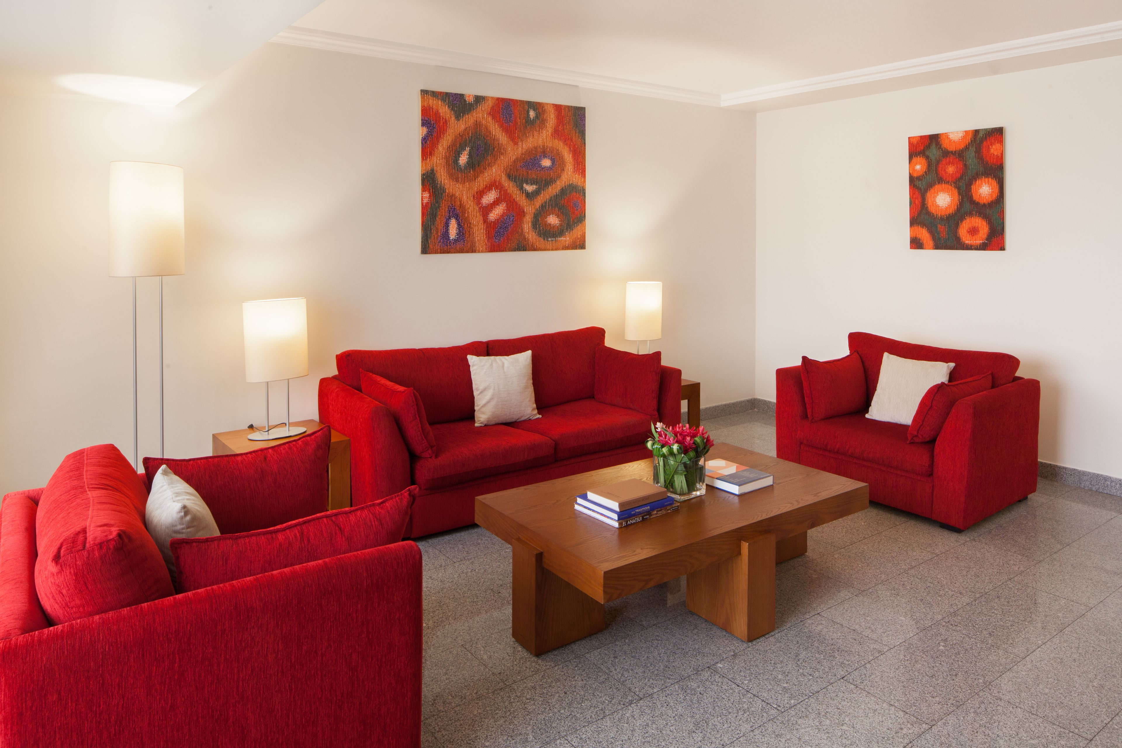 Ein modernes Wohnzimmer mit roten Sofas, einem Holztisch und zwei Wandleuchten.