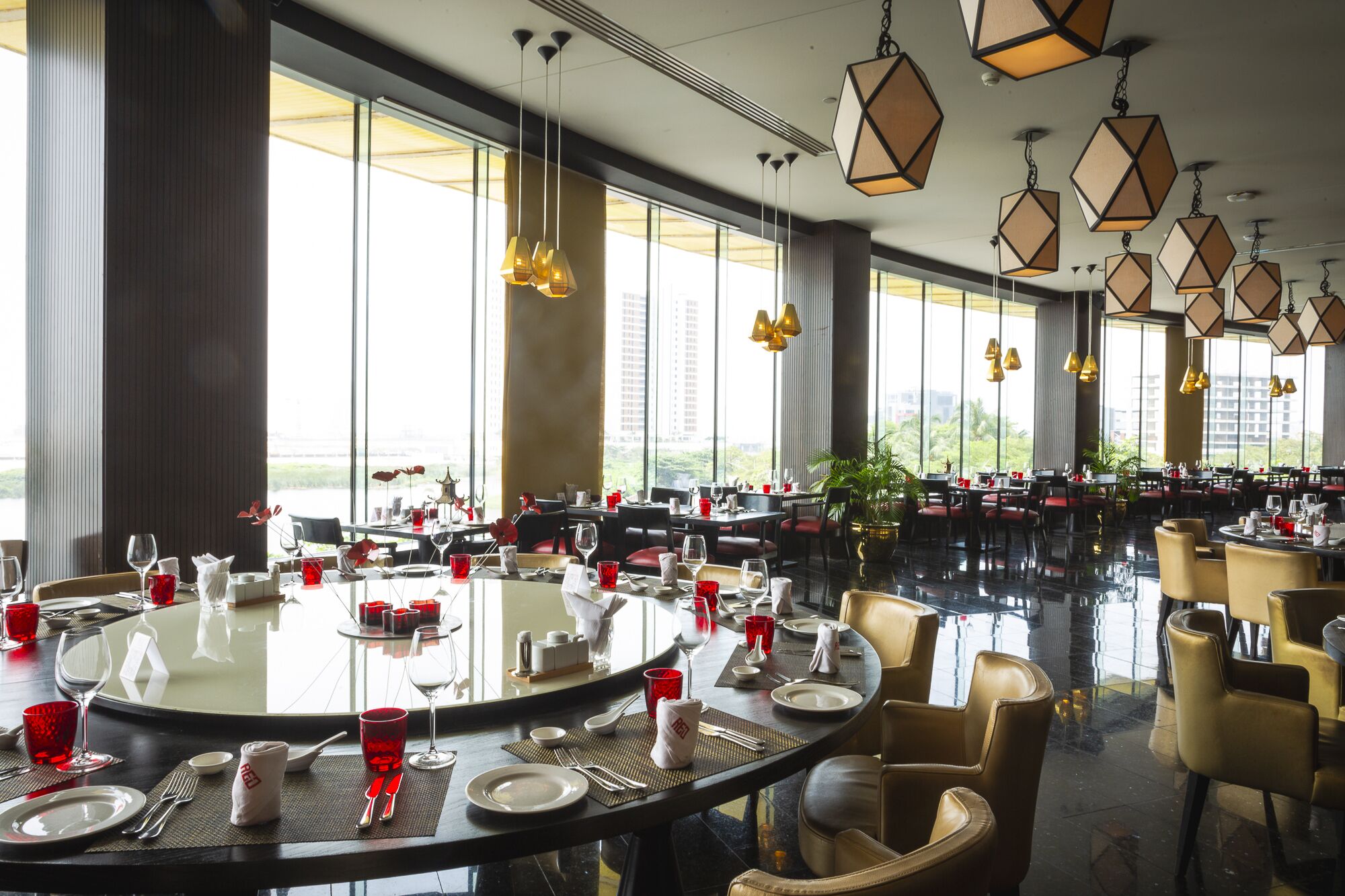 A spacious dining area with multiple round tables, each set with red glassware and white plates.