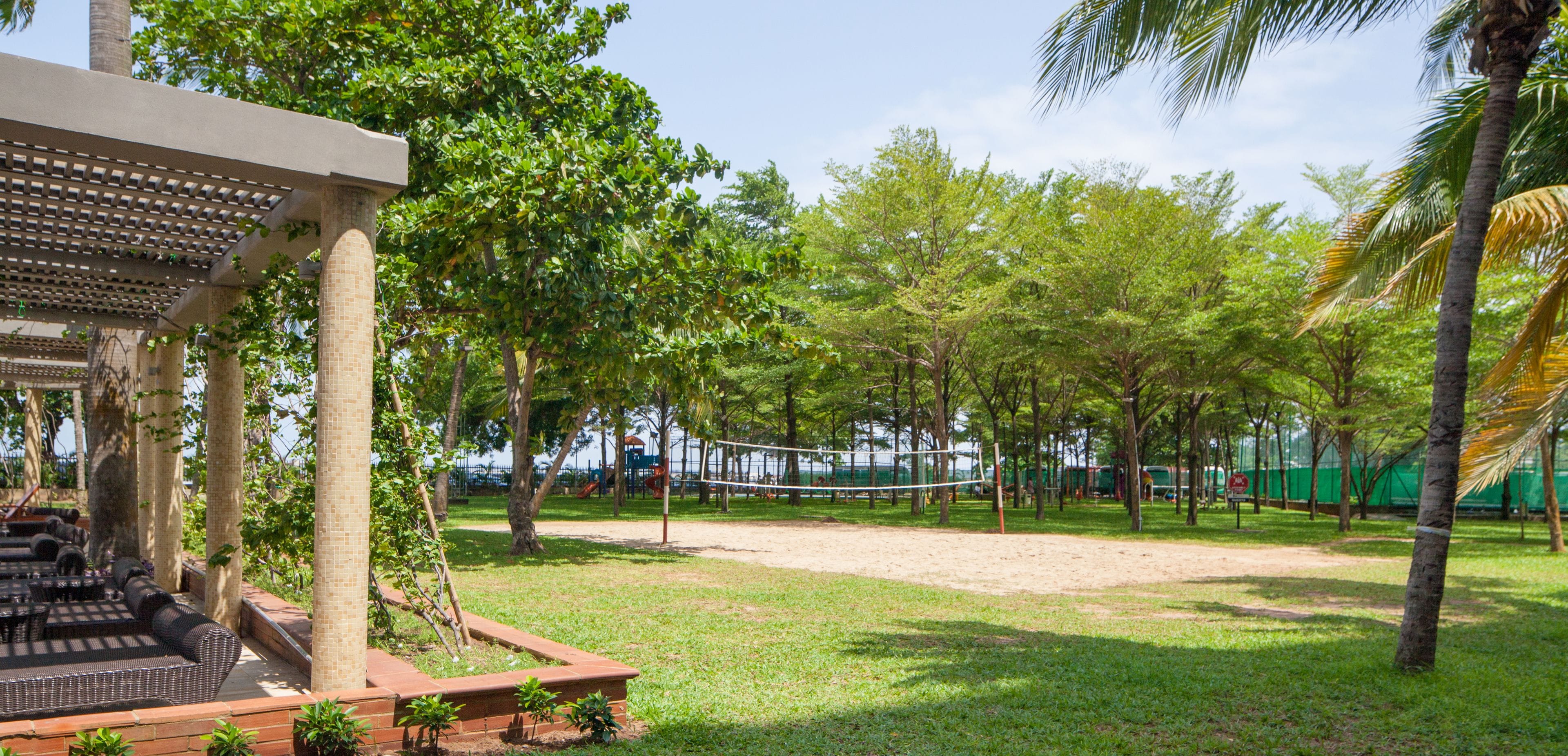 A park with a volleyball net, trees, and a covered seating area.