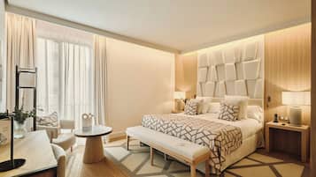 Una habitación de hotel moderna con una cama grande, mesitas de noche, un banco, una pequeña mesa redonda y un escritorio con una silla.