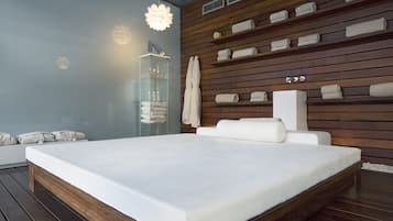 A modern bedroom with a large bed, wooden panel walls, and a glass cabinet with towels.