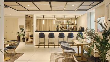 A modern kitchen with a bar area, featuring bar stools, a dining table, and potted plants.