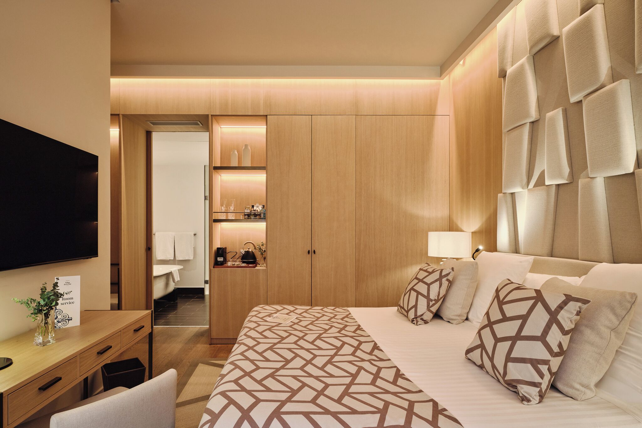 A hotel room with a large bed, a desk, a TV, and a wardrobe.