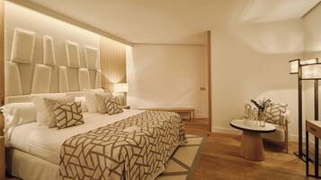 A modern bedroom with a large bed, bedside tables, a round wooden side table, and a chair.
