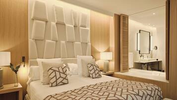 Habitación de hotel moderna con una cama grande, una mesita de noche con lámpara, cabecero integrado, un espejo y un baño con lavamanos y bañera.