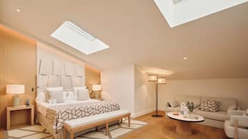 A modern bedroom with a skylight, a bed with a geometric-patterned bedspread, a bedside table with a lamp, a bench, a bedside table with a phone, a floor lamp, a sofa, and a coffee table with decorative items.