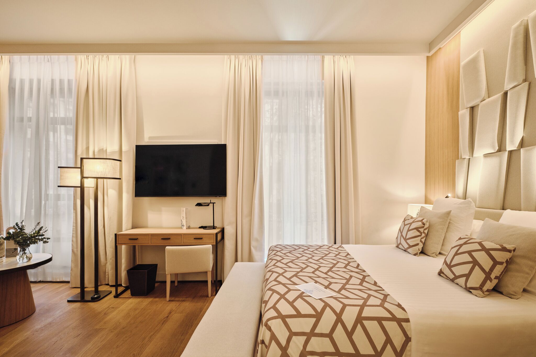 A hotel room with a bed, a desk, a chair, a TV, and curtains.