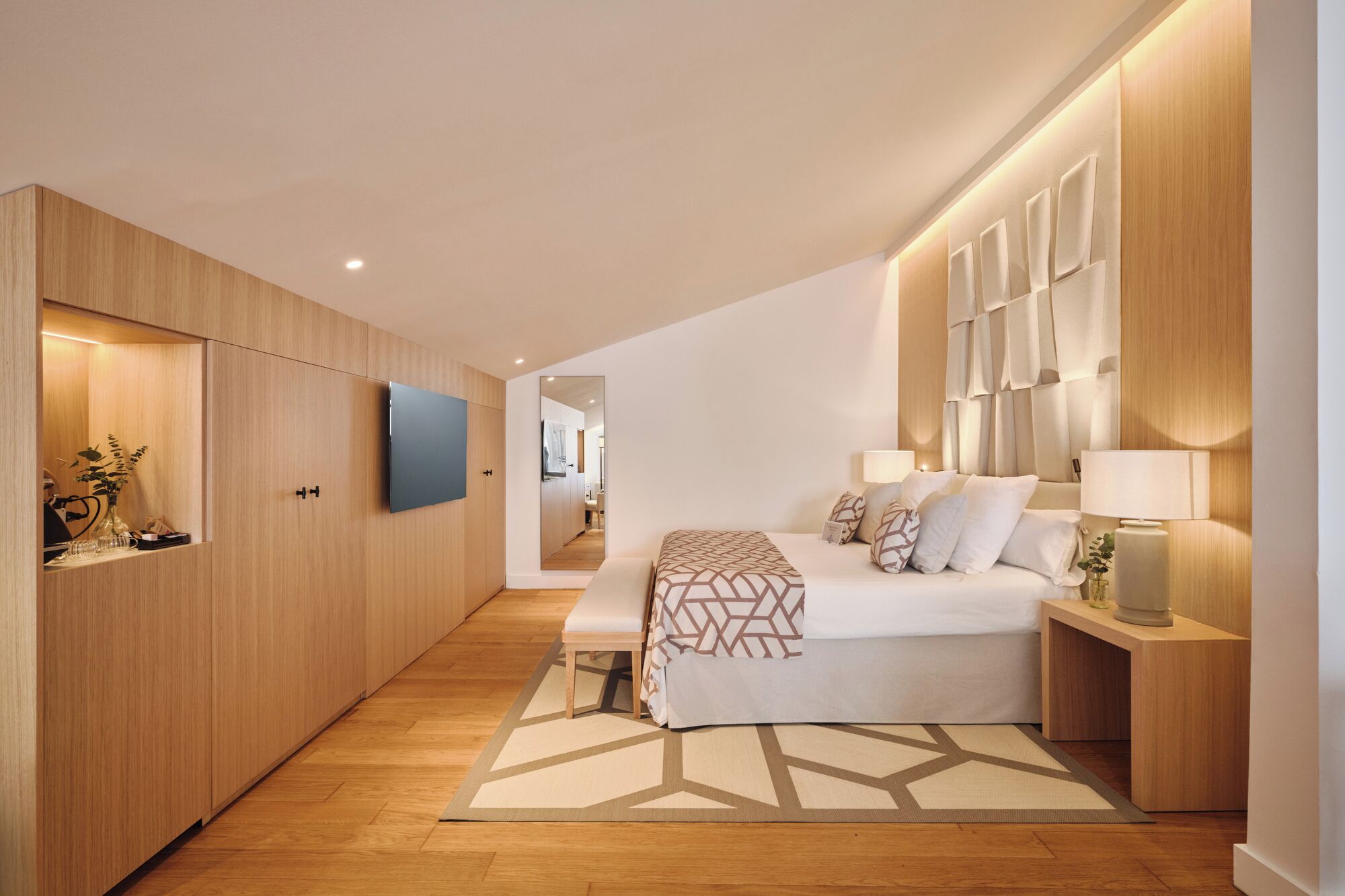 A modern bedroom with a large bed, bedside tables, a TV, and wooden paneling.