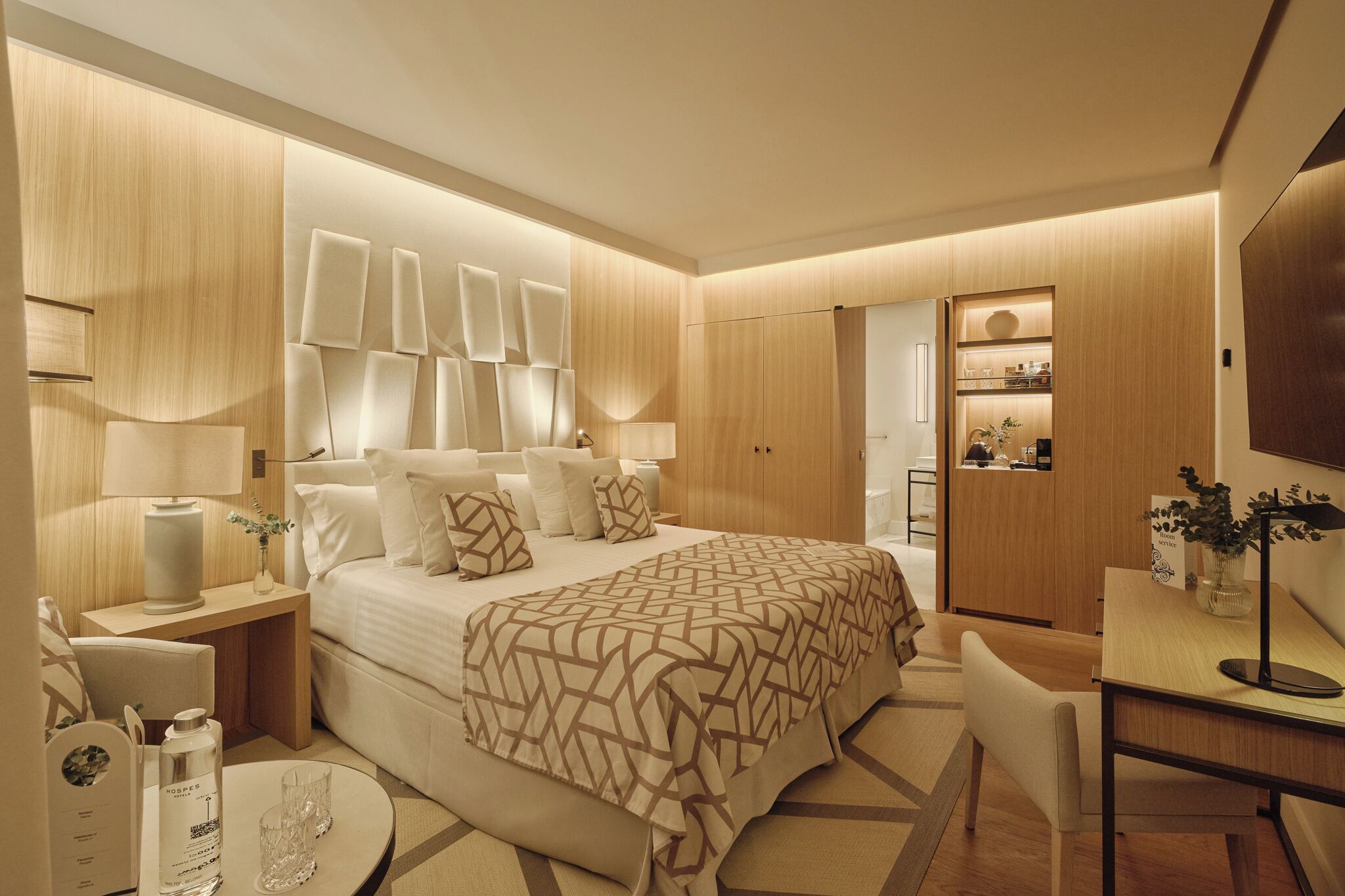 Quarto de hotel moderno com uma cama grande, mesas de cabeceira, uma escrivaninha e uma televisão.