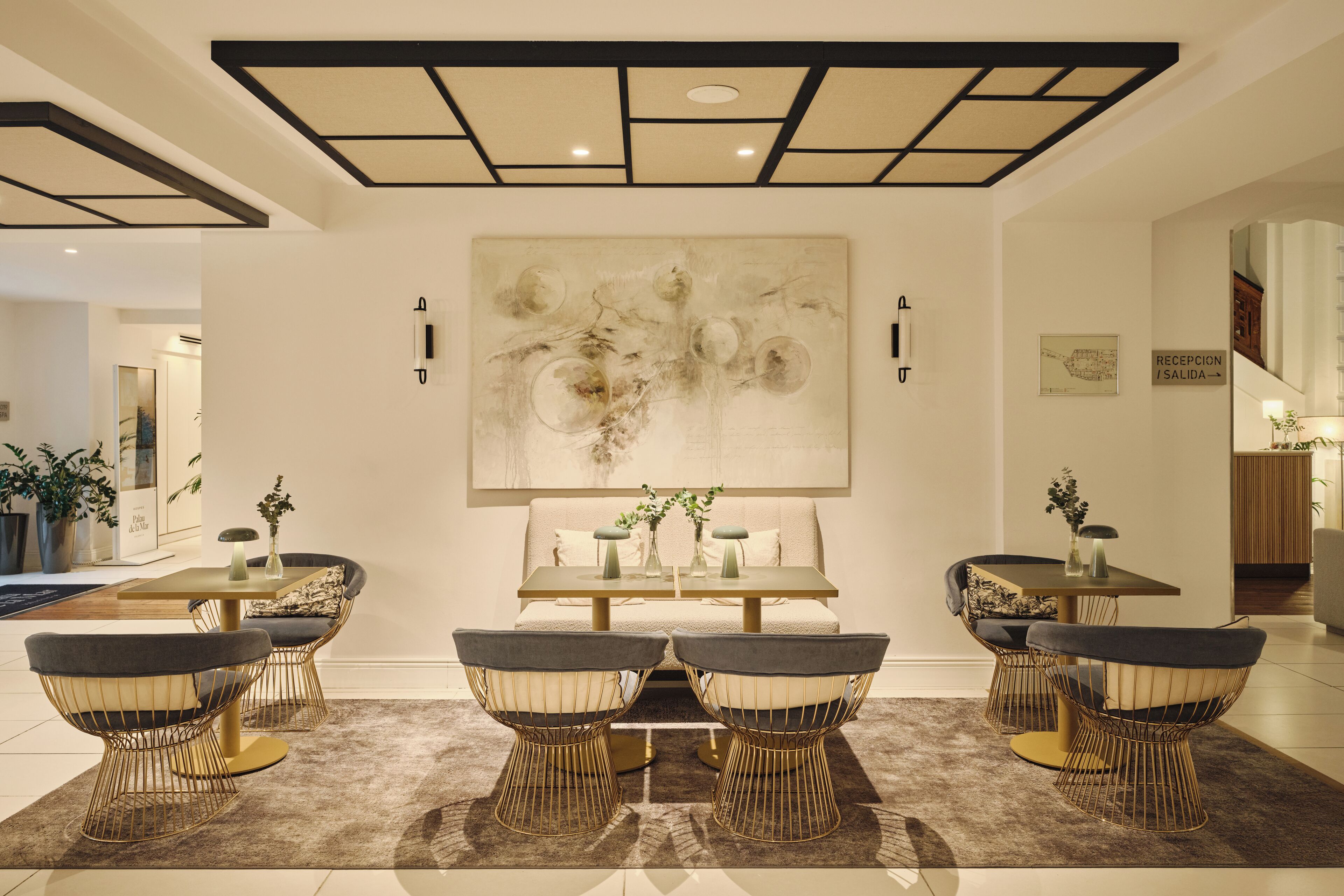 A modern dining area with a central table, surrounded by wireframe chairs with cushioned seats.