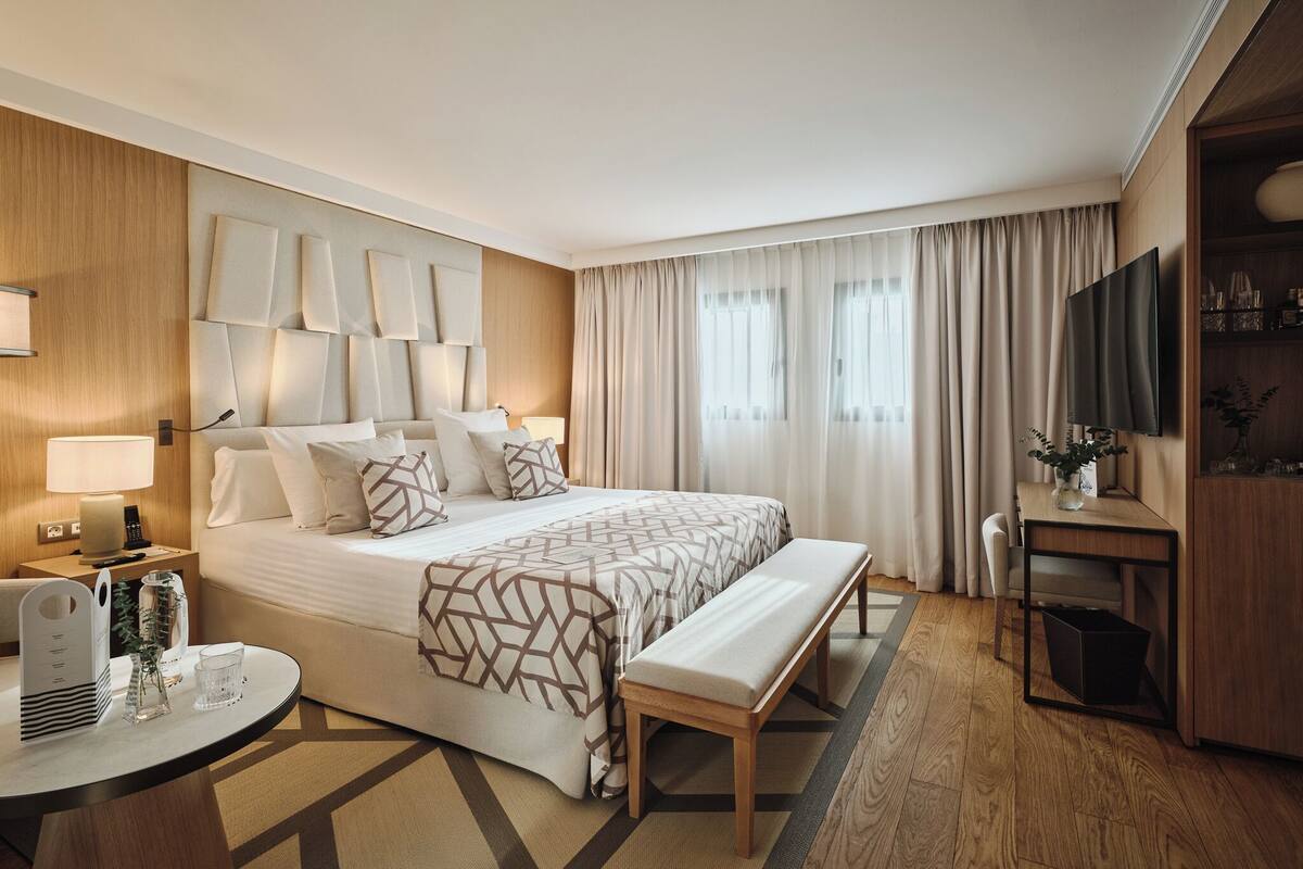Une chambre d’hôtel avec un grand lit, des tables de chevet, un bureau, un banc et un téléviseur.