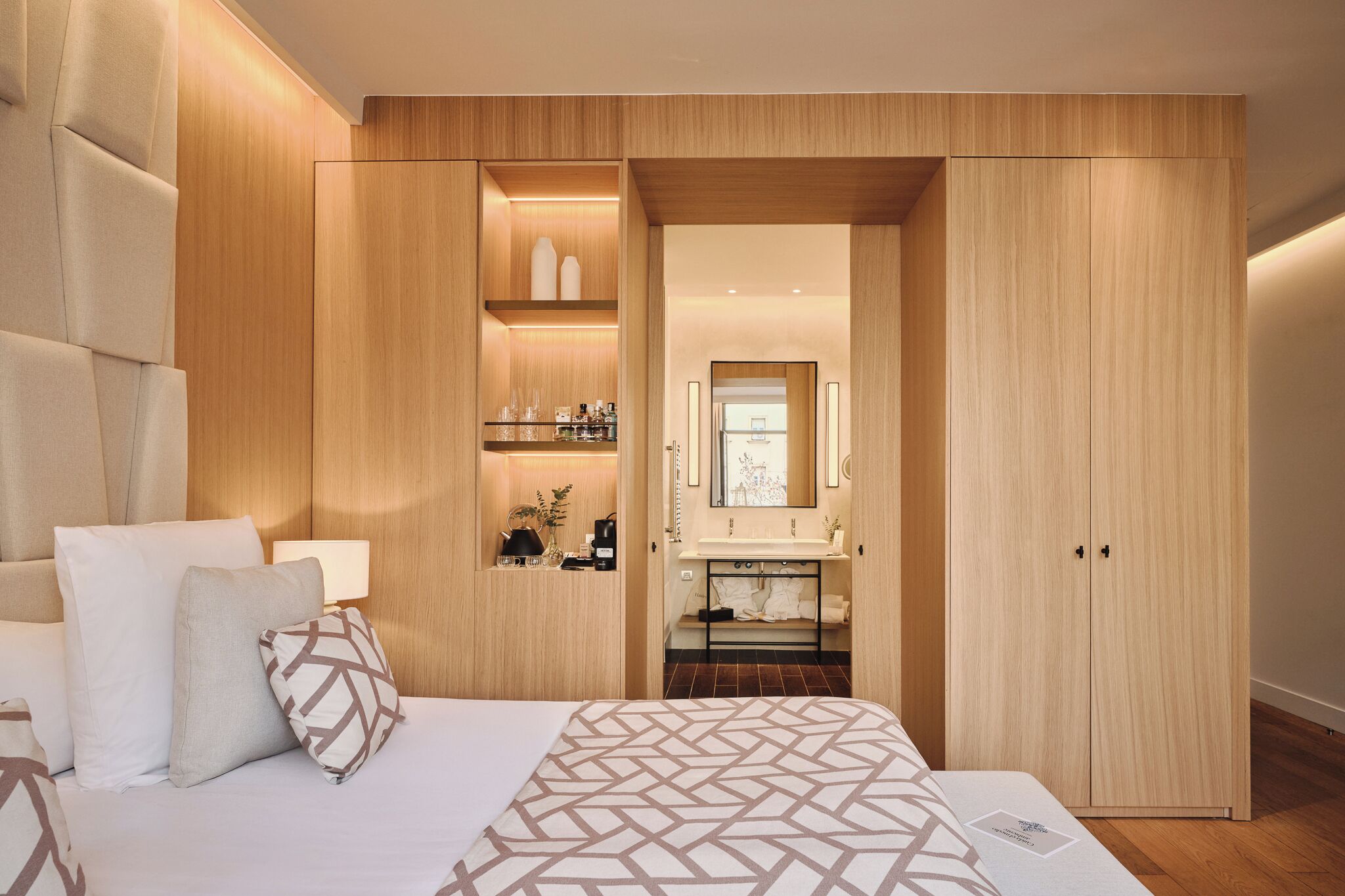 Une chambre d’hôtel moderne dotée d’un grand lit, d’une armoire intégrée, d’une coiffeuse avec un miroir et d’un petit coin salon avec une table et des chaises.