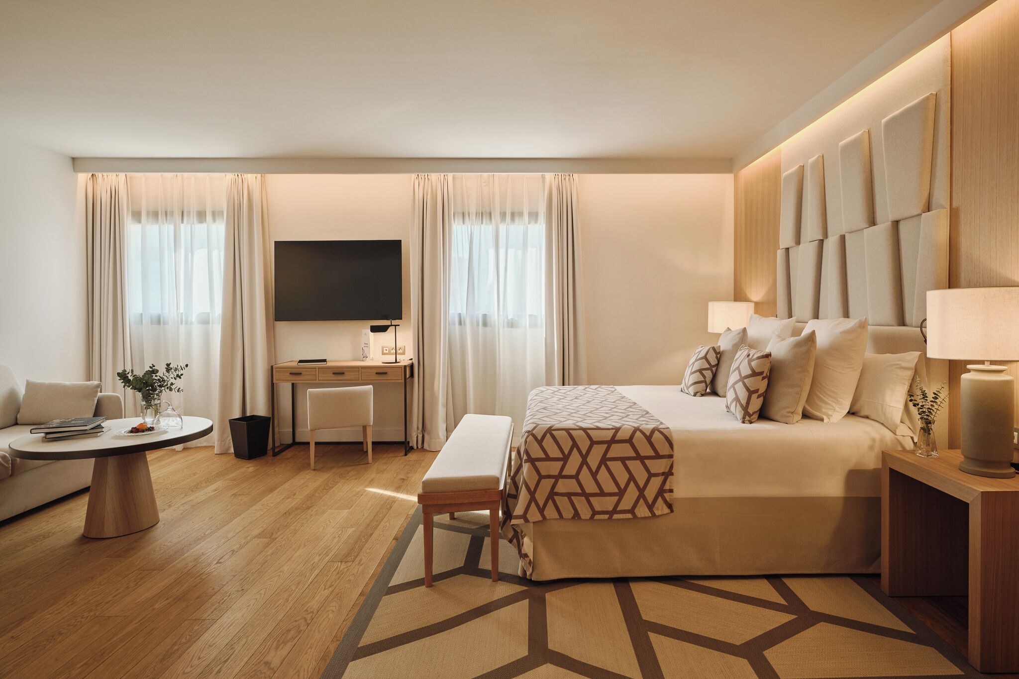 Habitación de hotel con cama, mesita de noche, lámpara, televisión, escritorio, silla y una pequeña mesa con una planta.