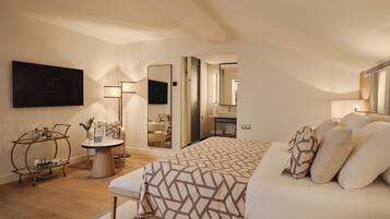Un dormitorio moderno con una cama grande, mesitas de noche, televisión y un baño visible a través de una puerta abierta.