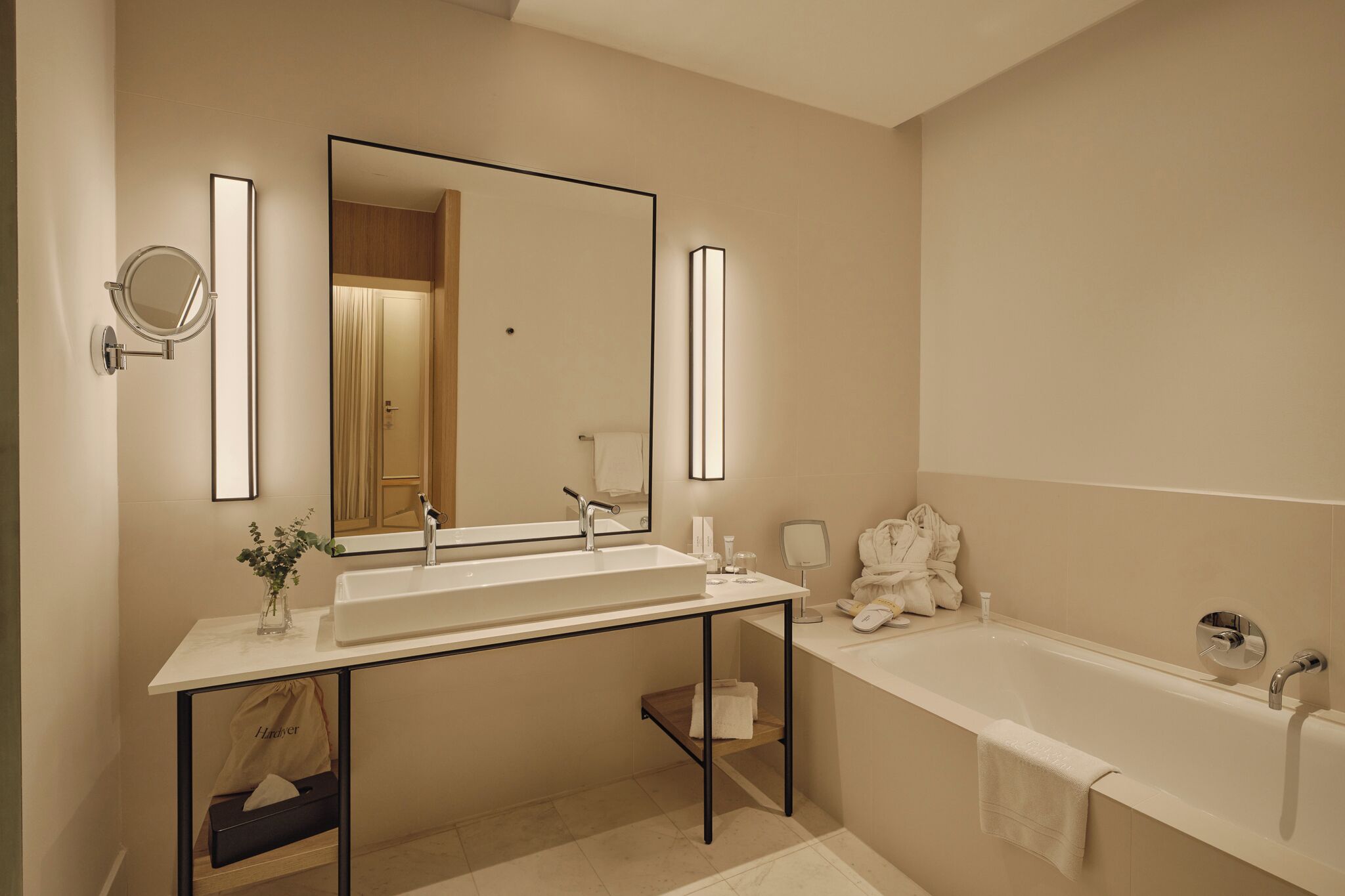 A modern bathroom with a large mirror, two sinks, a bathtub, and a vanity with a towel rack.