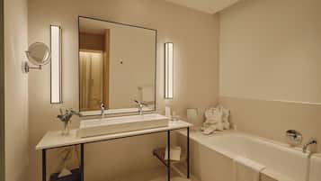 A modern bathroom with a large mirror, two sinks, a bathtub, and a vanity with a towel rack.