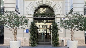 Une entrée imposante, avec un portail en arc de cercle, flanquée de deux grands arbres en pot, mène à un bâtiment à l’architecture classique, sur lequel on peut lire l’inscription « Palau de la Mar ».