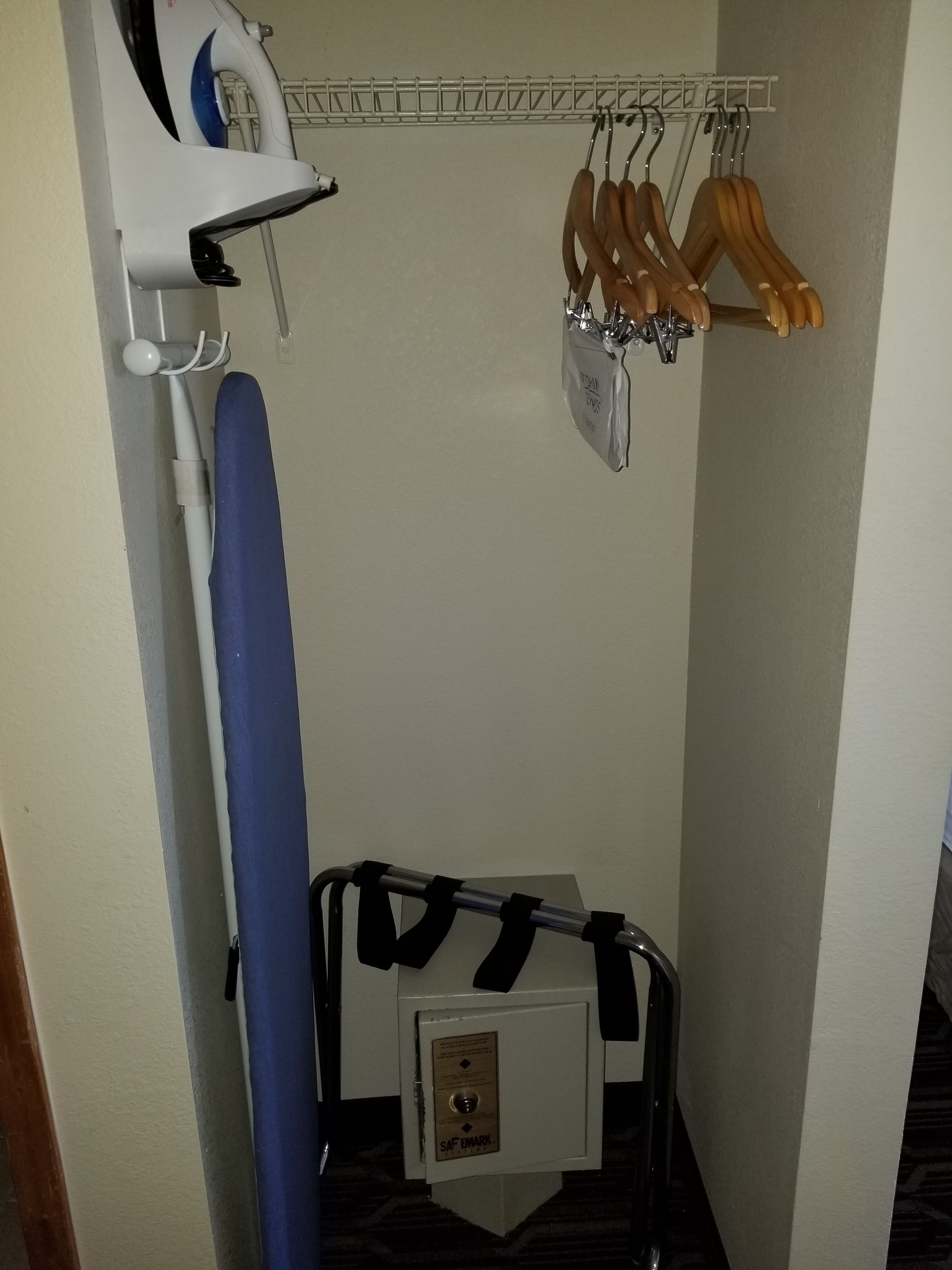 A small room with a blue ironing board, a white iron, and wooden hangers on a rack.