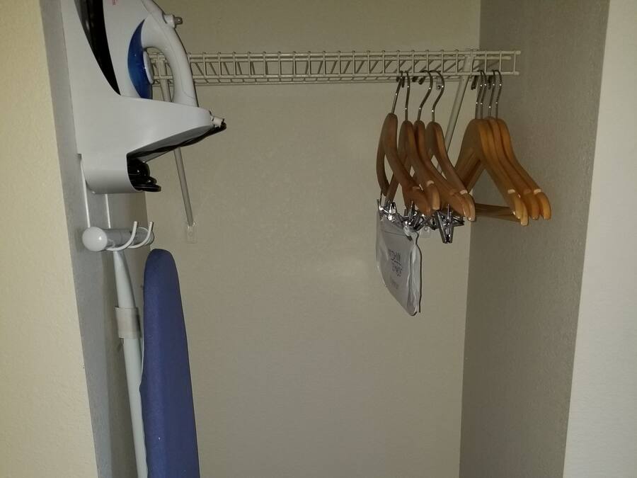 A small room with a blue ironing board, a white iron, and wooden hangers on a rack.