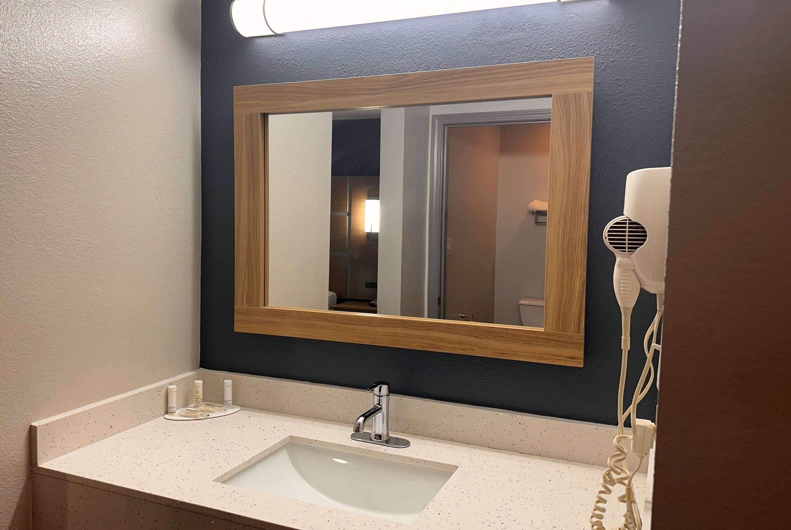 A bathroom with a large mirror, a sink, and a hairdryer on the counter.