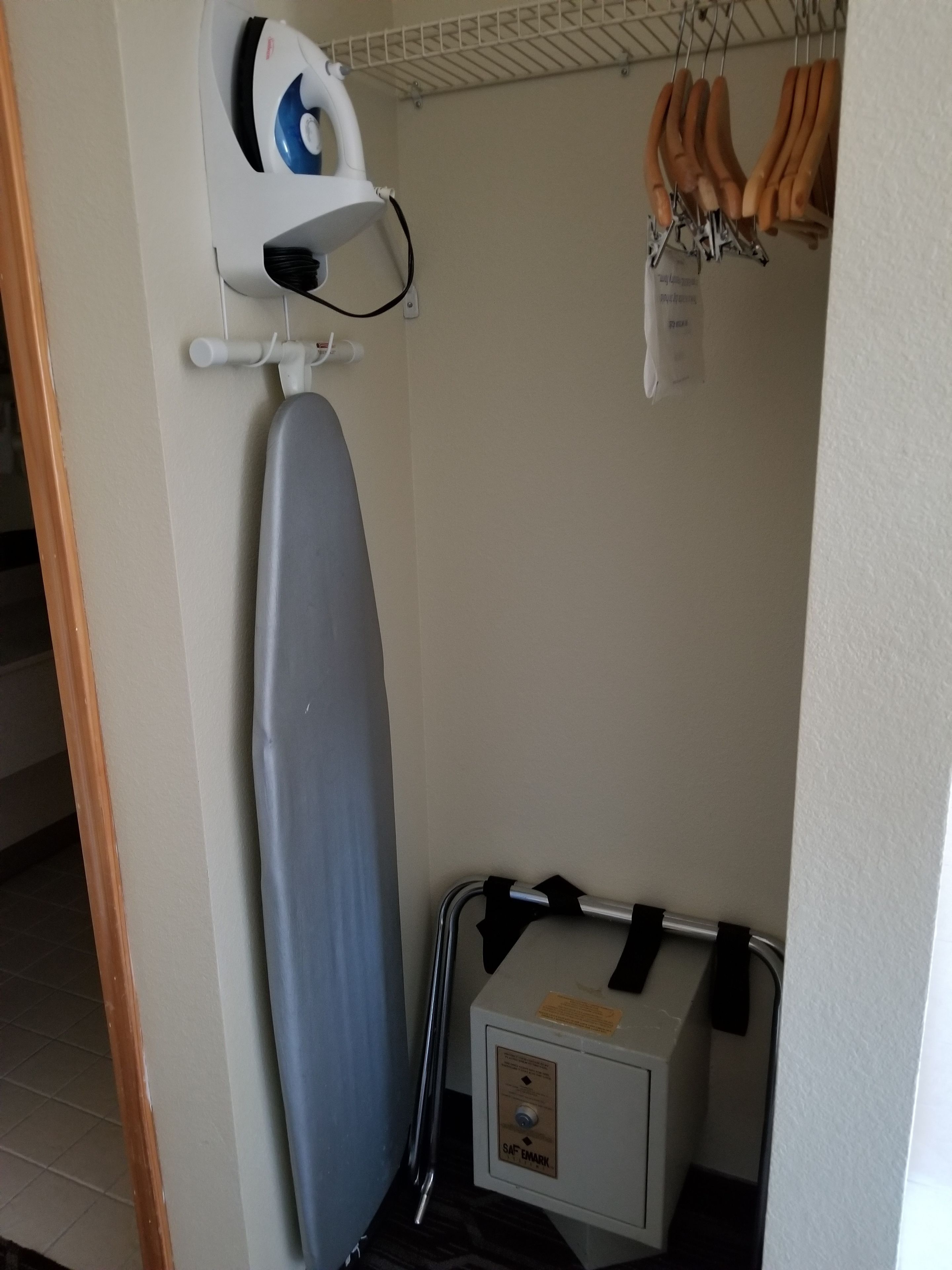 Una habitación compacta con una tabla de planchar fijada a la pared, un pequeño cofre de almacenamiento y una percha con elementos de madera.