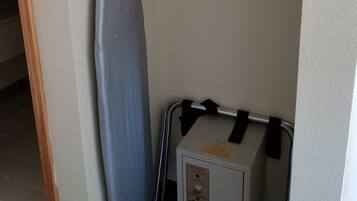 Una habitación compacta con una tabla de planchar fijada a la pared, un pequeño cofre de almacenamiento y una percha con elementos de madera.