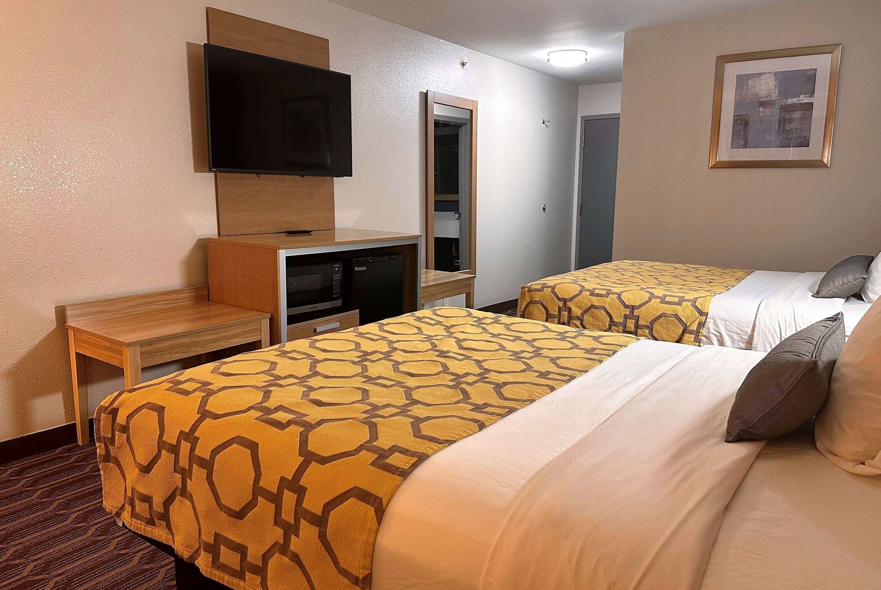 A hotel room with two beds, a TV, a desk, and a mirror.