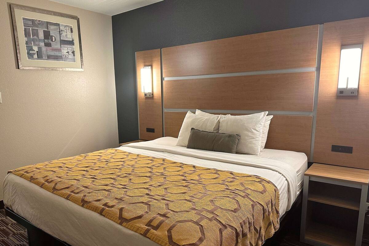 Ein Hotelzimmer mit einem großen Bett, einem Holzkopfteil, einem Nachttisch und einer Wandleuchte.