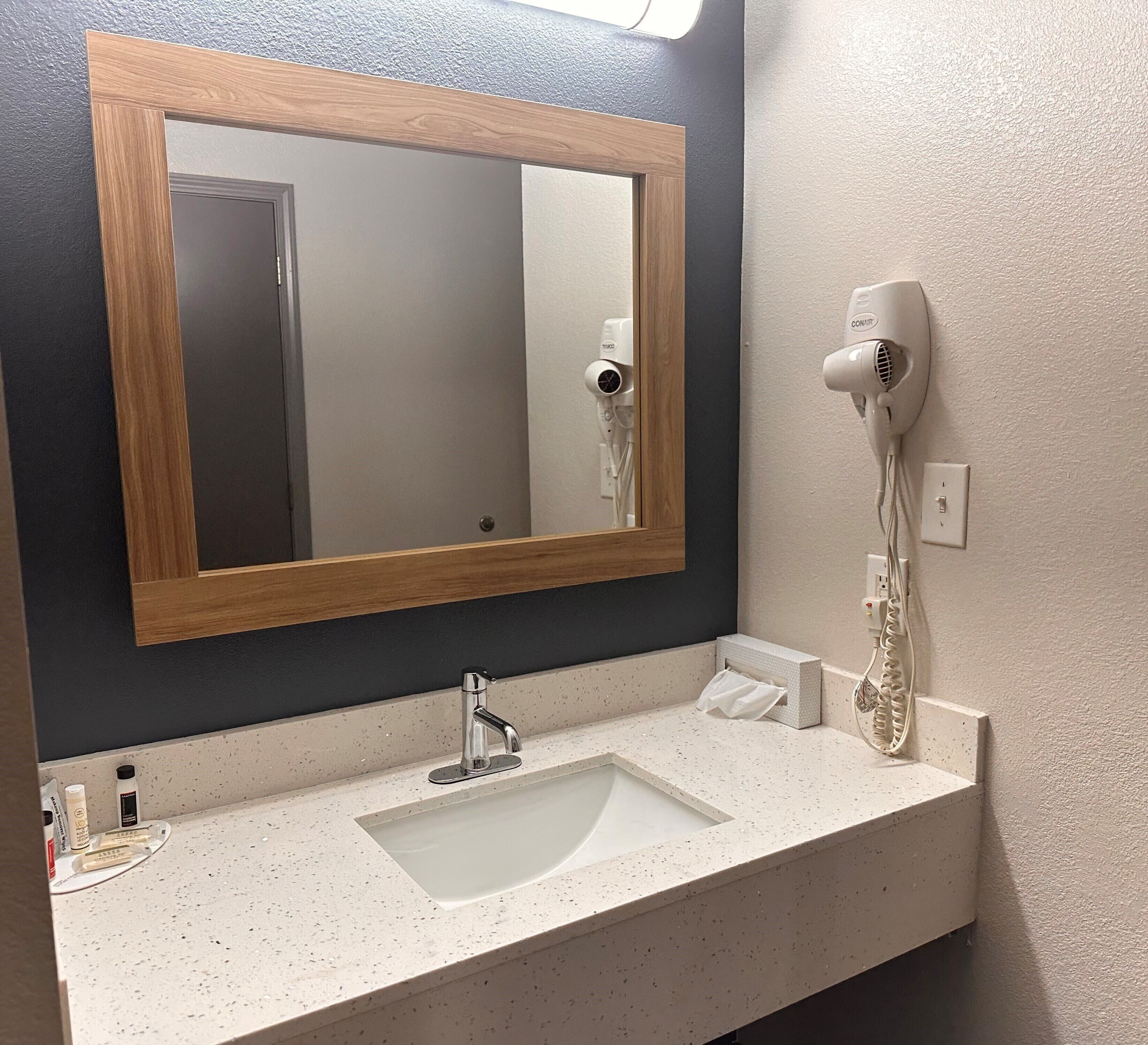 A bathroom with a wooden-framed mirror, a sink with a faucet, and a hairdryer mounted on the wall.