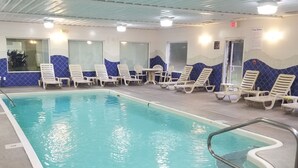 Une piscine intérieure à l’eau claire, entourée de chaises longues et bordée d’un mur carrelé orné d’un motif bleu.