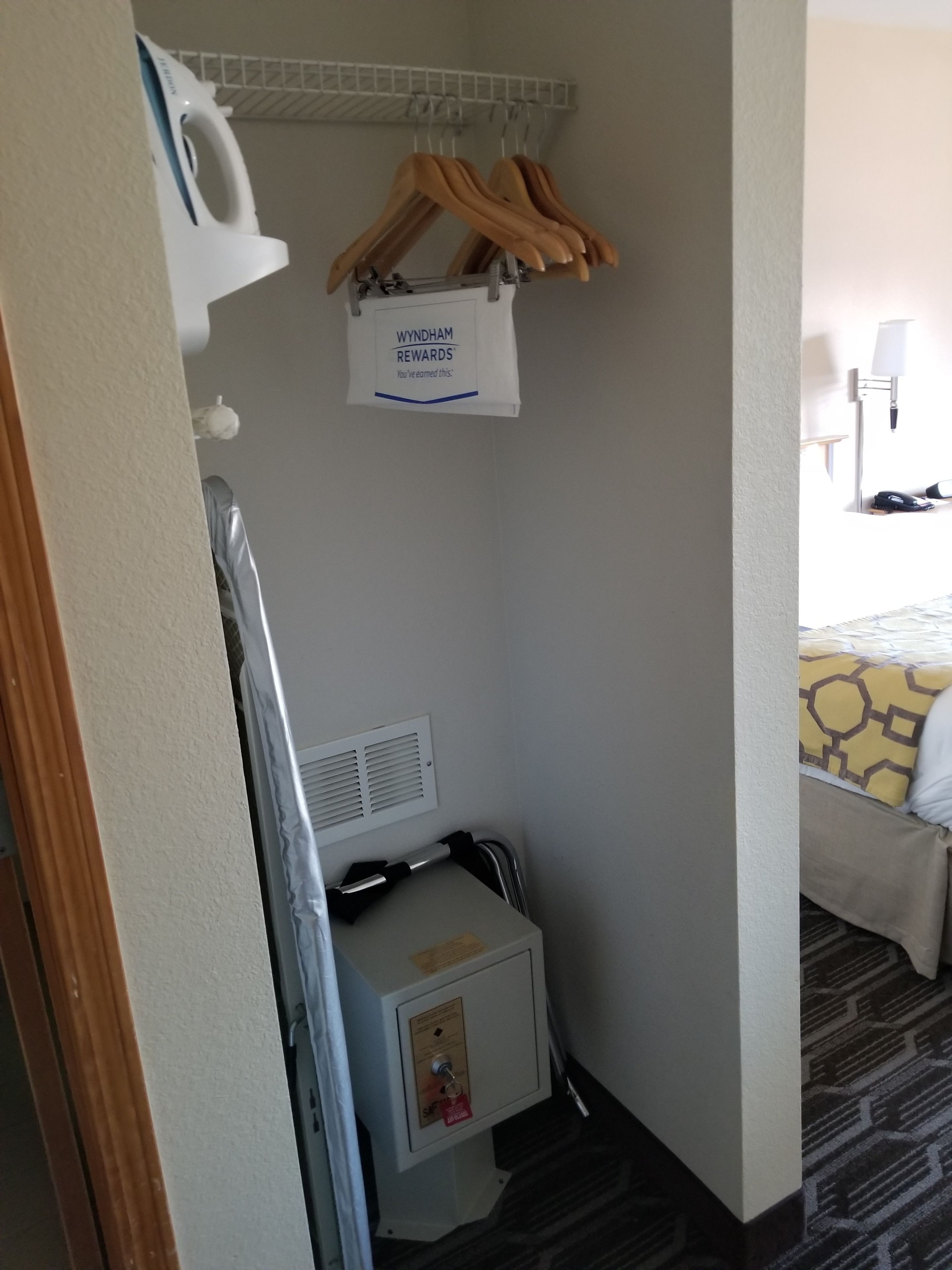 A compact hotel room with a small kitchenette, a wall-mounted heater, and a sign for Wyndham Rewards.