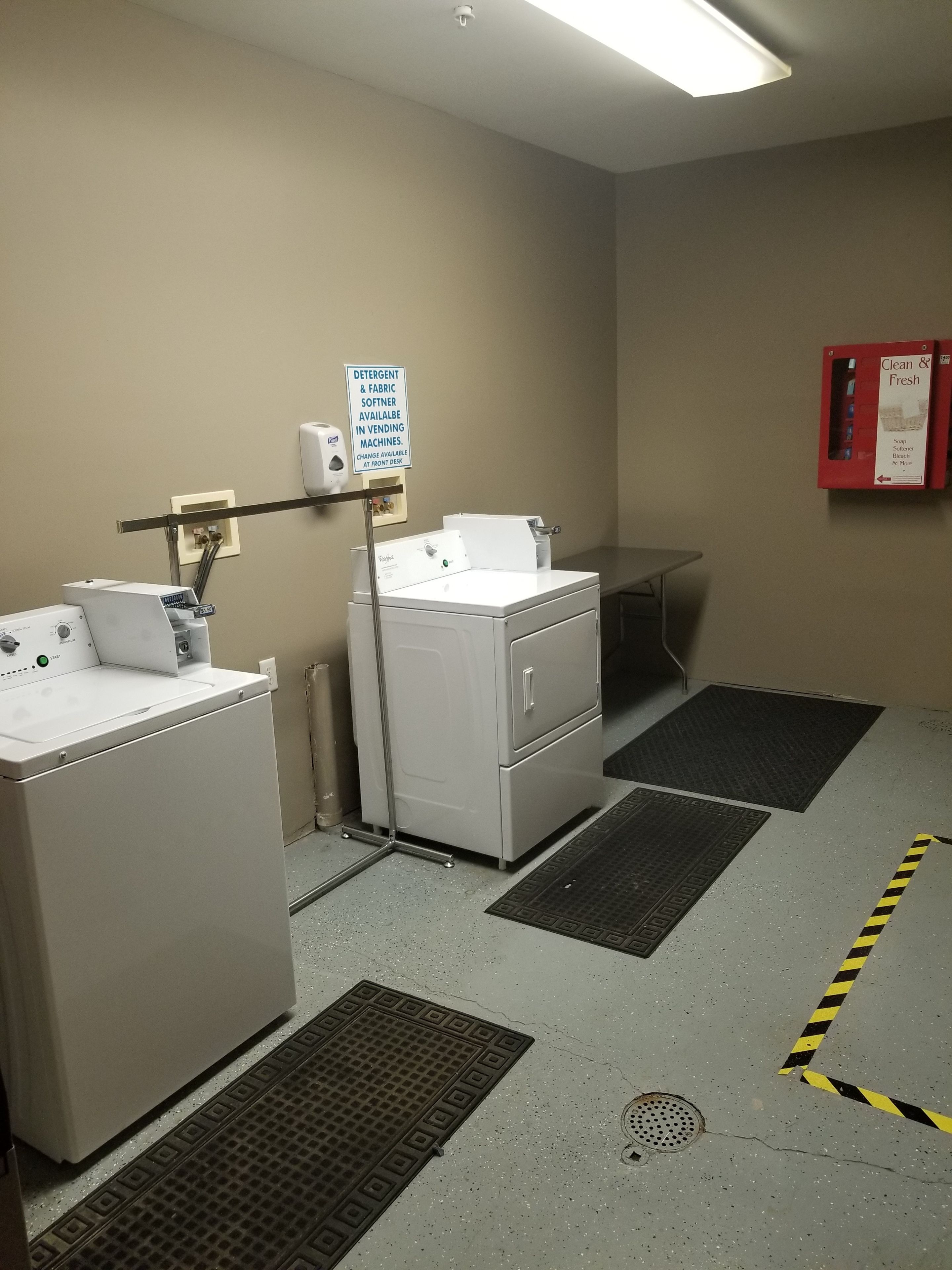 A laundry area with a washing machine, dryer, and a sign indicating detergent and fabric softener availability.