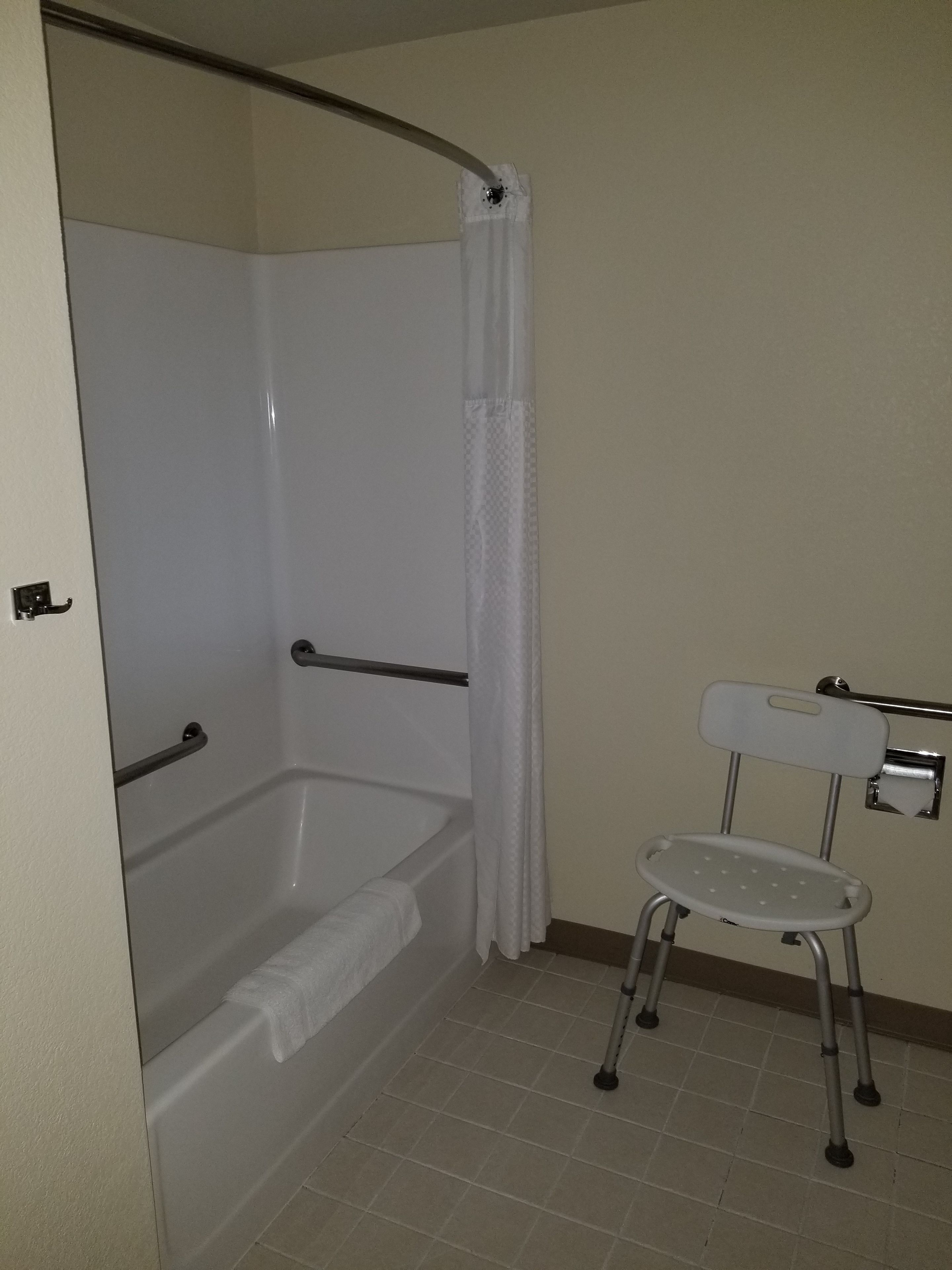 Une salle de bain équipée d’une baignoire, d’un rideau de douche, d’une barre d’appui, de toilettes avec un siège de sécurité et d’un porte-serviettes.