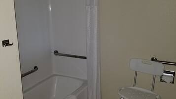 Casa de banho com banheira, cortina de chuveiro, barra de apoio, sanita com assento de segurança e suporte para toalhas.