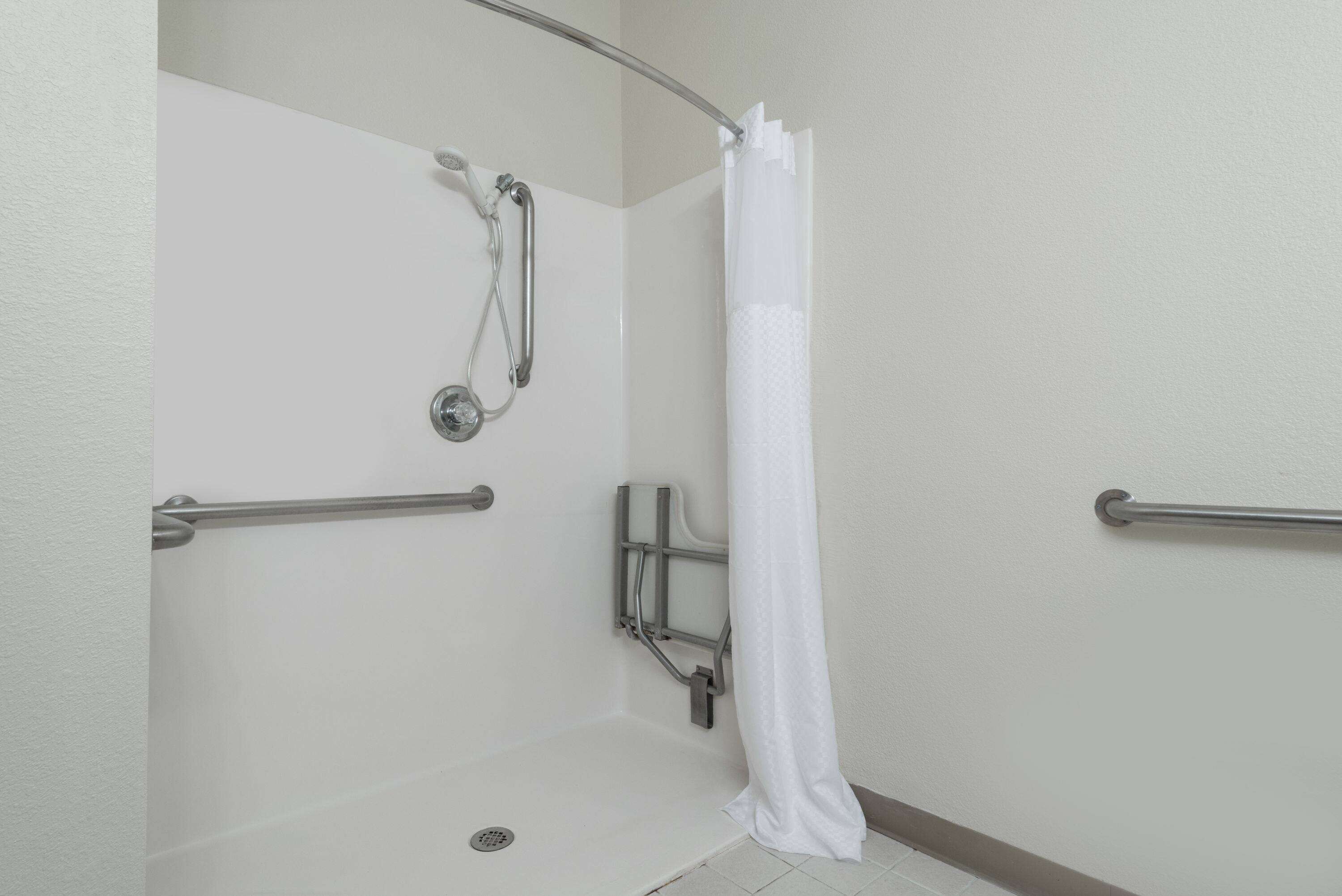 A shower area with a white shower curtain, grab bars, and a handheld showerhead.