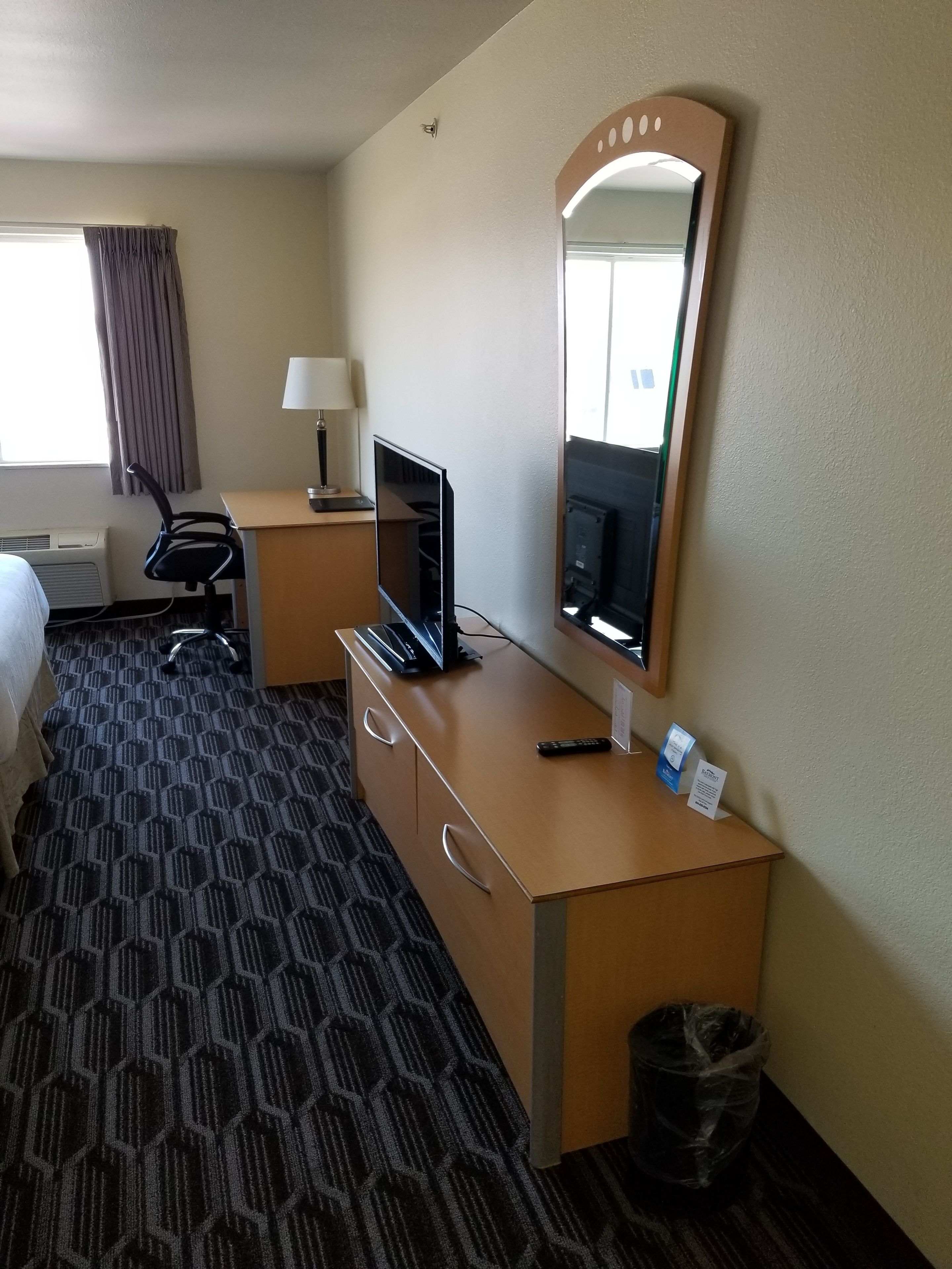 Une chambre d’hôtel équipée d’un lit, d’un bureau avec un ordinateur, d’une lampe, d’un miroir et d’une poubelle.