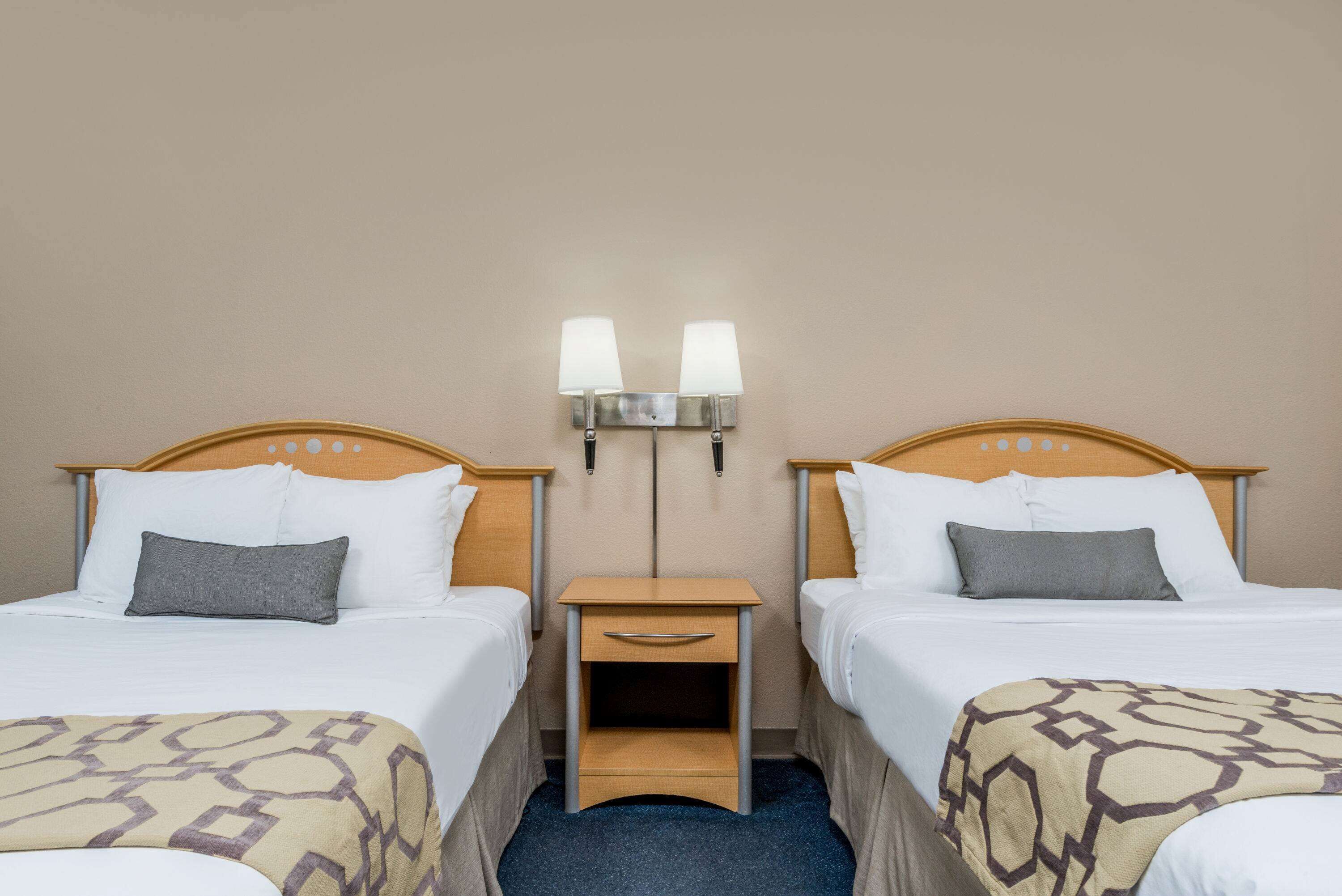 Una habitación de hotel con dos camas, una mesita de noche y una lámpara de pared entre ellas.