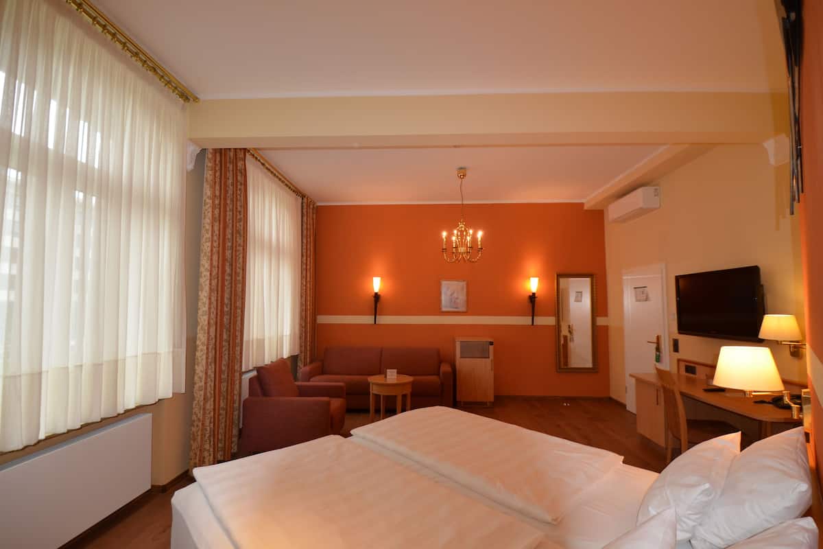 A hotel room with a bed, a desk, a chair, a sofa, and a television.