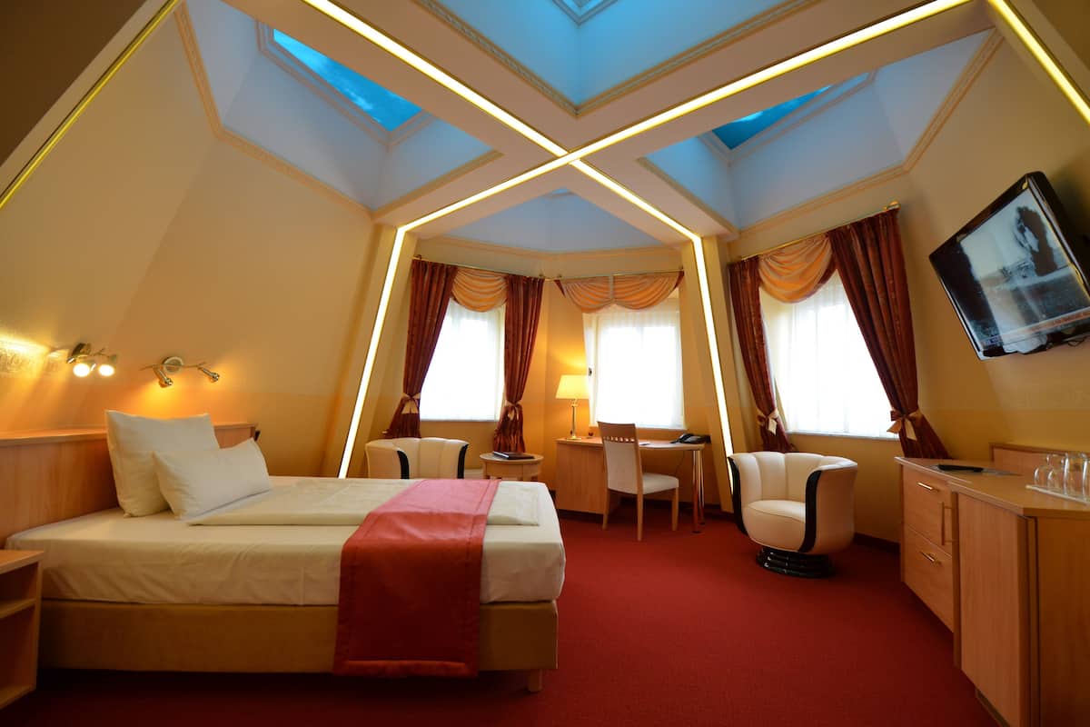 A hotel room with a bed, desk, chair, and TV.